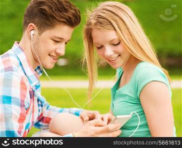 summer, vacation, holidays, technology and friendship concept - smiling couple with smartphone and earphones sitting in park