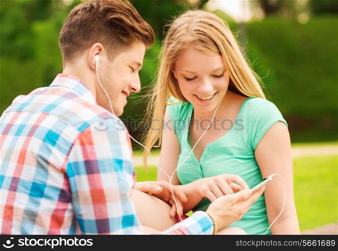 summer, vacation, holidays, technology and friendship concept - smiling couple with smartphone and earphones sitting in park