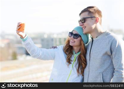 summer, vacation, holidays, technology and friendship concept - smiling couple with smartphone taking selfie outdoors