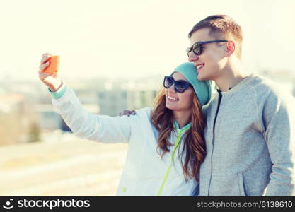 summer, vacation, holidays, technology and friendship concept - smiling couple with smartphone taking selfie outdoors