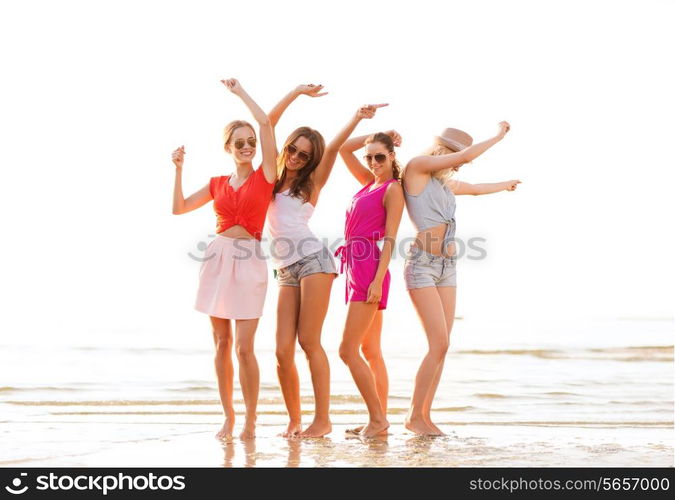 summer vacation, holidays, travel and people concept - group of smiling young women in sunglasses and casual clothes dancing on beach