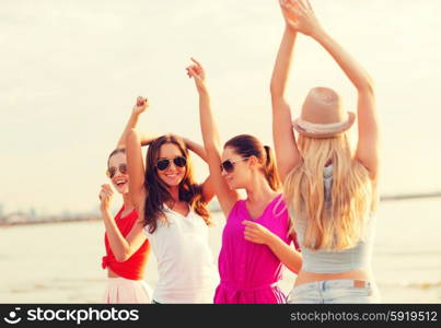 summer vacation, holidays, travel and people concept - group of smiling young women in sunglasses and casual clothes dancing on beach