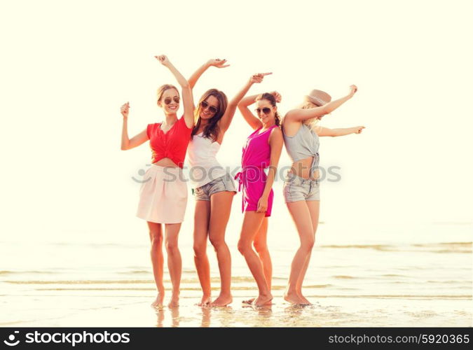 summer vacation, holidays, travel and people concept - group of smiling young women in sunglasses and casual clothes dancing on beach