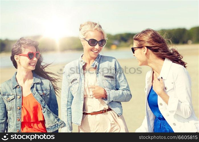 summer vacation, holidays, travel and people concept - group of smiling young female friends in sunglasses and casual clothes walking along beach. group of smiling young female friends on beach