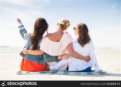 summer vacation, holidays, travel and people concept - group of young women sitting on beach blanket and pointing finger to something