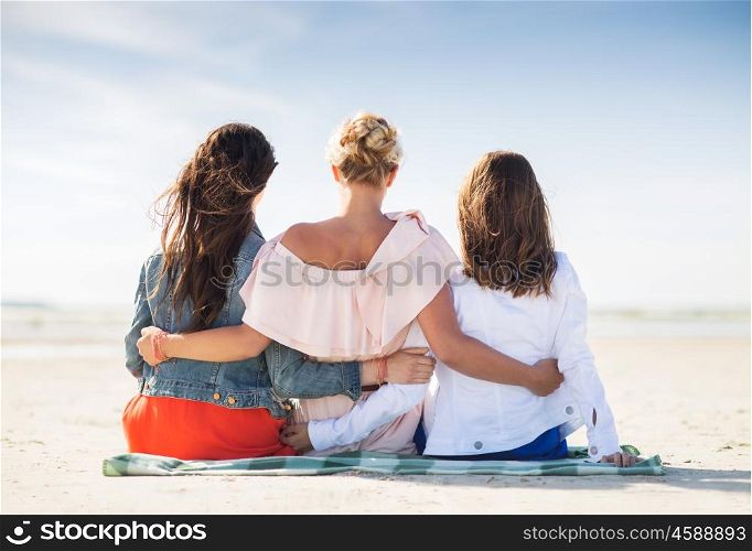 summer vacation, holidays, travel and people concept - group of young women in casual clothes hugging sitting on beach blanket