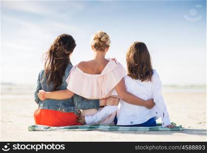 summer vacation, holidays, travel and people concept - group of young women in casual clothes hugging sitting on beach blanket