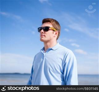 summer vacation, holidays, travel and people concept - young man in sunglasses at summer beach or seaside
