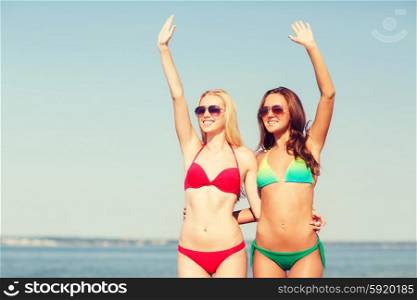summer vacation, holidays, travel, gesture and people concept - two smiling young women waving hands on beach