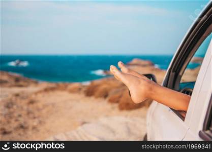 Summer vacation, holidays, travel, road trip and people concept - close up of feet showing from car window. Closeup of little girl feet showing from car window