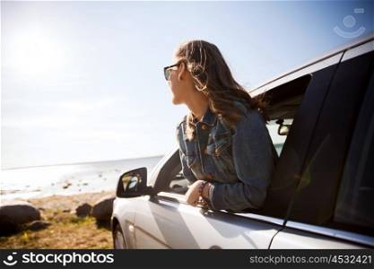 summer vacation, holidays, travel, road trip and people concept - happy smiling teenage girl or young woman in car at seaside