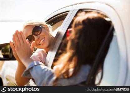 summer vacation, holidays, travel, road trip and people concept - happy teenage girls or young women in car at seaside making high five gesture