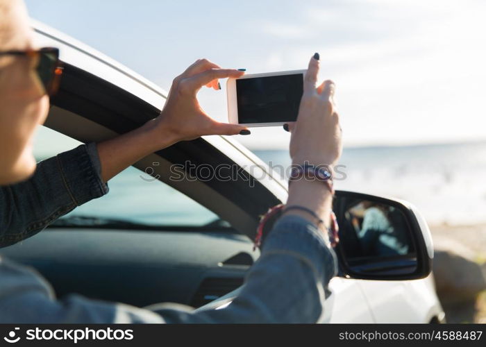 summer vacation, holidays, travel, road trip and people concept - happy teenage girl or young woman in car taking picture of sea with smartphone