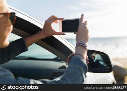 summer vacation, holidays, travel, road trip and people concept - happy teenage girl or young woman in car taking picture of sea with smartphone