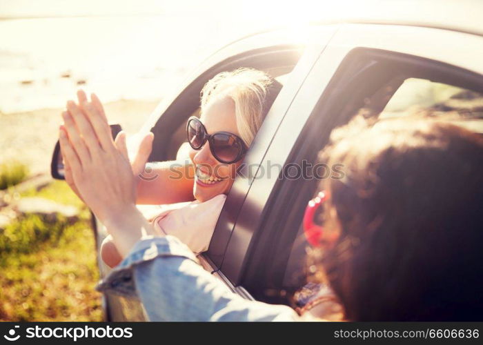 summer vacation, holidays, travel, road trip and people concept - happy teenage girls or young women in car at seaside making high five gesture. happy teenage girls or women in car at seaside