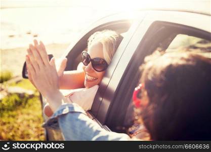 summer vacation, holidays, travel, road trip and people concept - happy teenage girls or young women in car at seaside making high five gesture. happy teenage girls or women in car at seaside