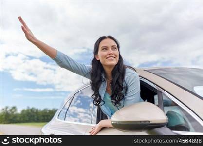 summer vacation, holidays, travel, road trip and people concept - happy young woman driving in car and waving hand