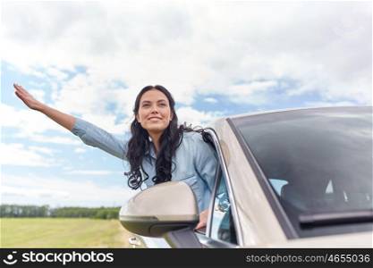 summer vacation, holidays, travel, road trip and people concept - happy young woman driving in car and waving hand