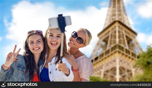 summer vacation, holidays, travel, technology and people concept- group of smiling young women taking picture with smartphone on selfie stick over eiffel tower in paris background