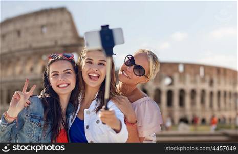 summer vacation, holidays, travel, technology and people concept- group of smiling young women taking picture with smartphone on selfie stick over coliseum in rome background
