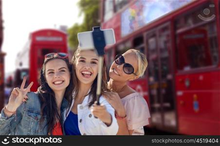 summer vacation, holidays, travel, technology and people concept- group of smiling young women taking picture with smartphone on selfie stick over london city street background