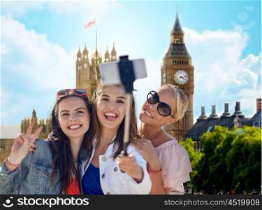 summer vacation, holidays, travel, technology and people concept- group of smiling young women taking picture with smartphone on selfie stick over london city and big ben tower background