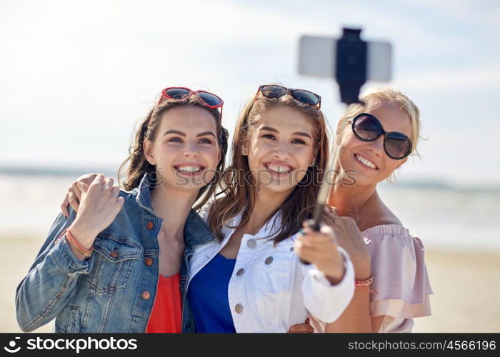 summer vacation, holidays, travel, technology and people concept- group of smiling young women taking picture with smartphone on selfie stick on beach