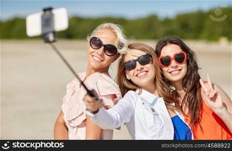 summer vacation, holidays, travel, technology and people concept- group of smiling young women taking picture with smartphone on selfie stick on beach