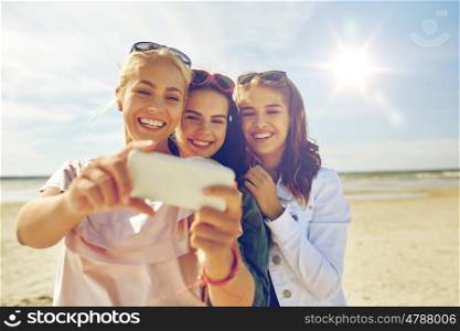 summer vacation, holidays, travel, technology and people concept- group of smiling young women taking sulfide with smartphone on beach