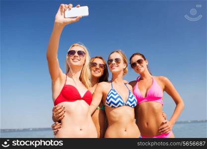 summer vacation, holidays, travel, technology and people concept- group of smiling young women on beach making selfie with smartphone over blue sky background