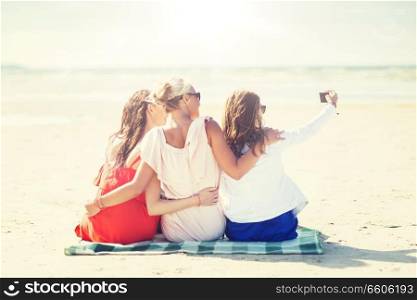 summer vacation, holidays, travel, technology and people concept- group of smiling young women taking selfie with smartphone on beach. happy women taking selfie by smartphone on beach