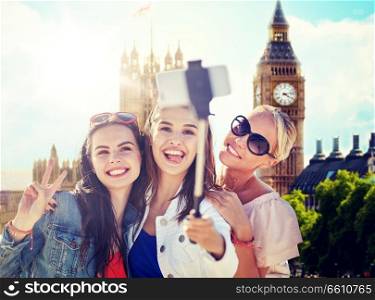 summer vacation, holidays, travel, technology and people concept- group of smiling young women taking picture with smartphone on selfie stick over london city and big ben tower background. group of smiling women taking selfie in london