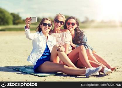 summer vacation, holidays, travel, technology and people concept- group of smiling young women taking selfie with smartphone on beach. group of smiling women taking selfie on beach