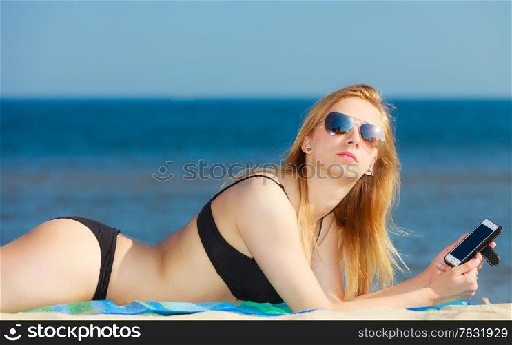Summer vacation. Sexy girl in bikini sunbathing tanning on the beach. Young woman relaxing with mobile phone on the sea coast. Summertime.