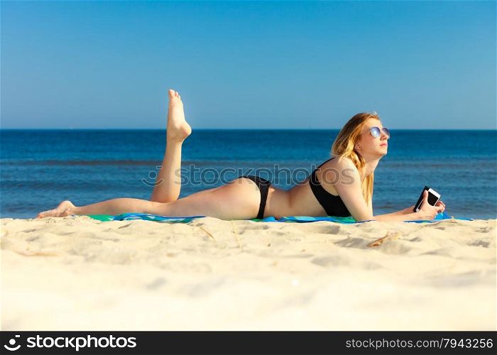 Summer vacation. Sexy girl in bikini sunbathing tanning on the beach. Young woman relaxing with mobile phone on the sea coast. Summertime.
