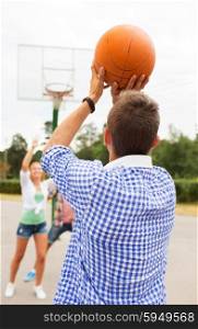 summer vacation, sport, games and friendship concept - group of happy teenagers playing basketball outdoors from back