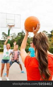 summer vacation, sport, games and friendship concept - group of happy teenagers playing basketball outdoors from back
