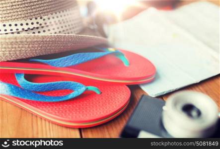 summer vacation, tourism and objects concept - close up of travel map, flip-flops, hat and camera. close up of travel map, flip-flops, hat and camera