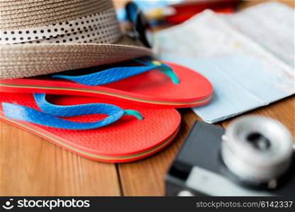 summer vacation, tourism and objects concept - close up of travel map, flip-flops, hat and camera