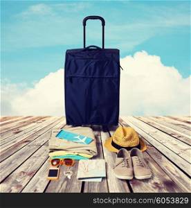 summer vacation, tourism and objects concept - travel bag, map, air ticket and clothes with personal stuff over wooden floor and blue sky background