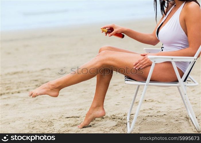 summer vacation, tourism, travel, holidays and people concept - close up of woman sunbathing in lounge and spraying sunscreen oil on beach