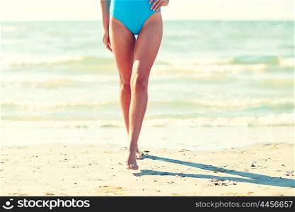 summer vacation, tourism, travel, holidays and people concept -close up of young woman in swimsuit walking on beach from back