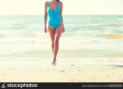 summer vacation, tourism, travel, holidays and people concept -close up of young woman in swimsuit walking on beach from back