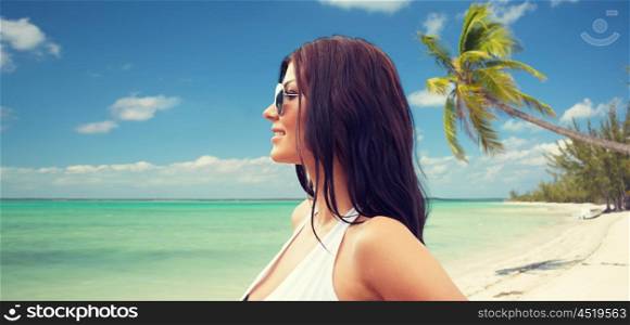 summer vacation, tourism, travel, holidays and people concept -face of smiling young woman in swimsuit with sunglassesover tropical beach background