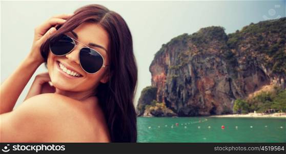 summer vacation, tourism, travel, holidays and people concept -face of smiling young woman with sunglasses over sea and island rock at tropical beach on bali background
