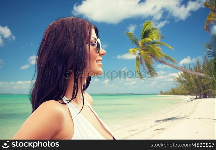 summer vacation, tourism, travel, holidays and people concept -face of smiling young woman in swimsuit with sunglassesover tropical beach background