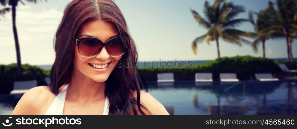 summer vacation, tourism, travel, holidays and people concept -face of smiling young woman with sunglasses over resort beach with palms and swimming pool background