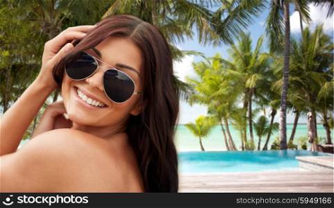 summer vacation, tourism, travel, holidays and people concept -face of smiling young woman with sunglasses over hotel resort swimming pool on beach background