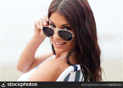 summer vacation, tourism, travel, holidays and people concept -face of smiling young woman with sunglasses sunbathing in lounge or folding chair on beach