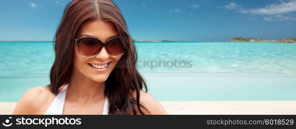 summer vacation, tourism, travel, holidays and people concept -face of smiling young woman with sunglasses over tropical beach background